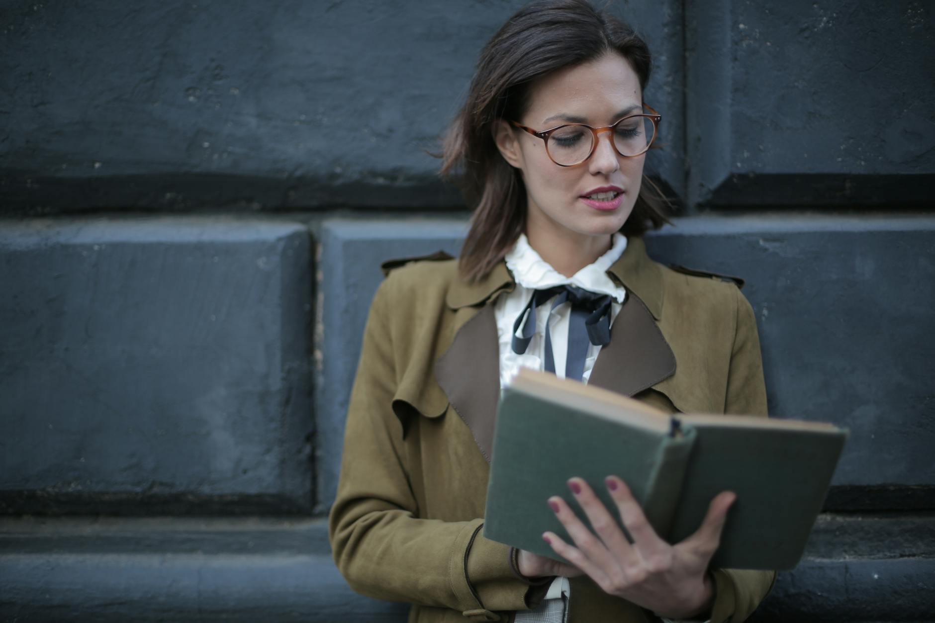 photo of woman in brown coat and glasses reading a book